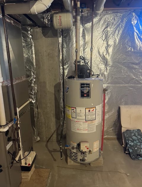 Basement utility room with a large white cylindrical water heater surrounded by insulation and ductwork piping